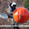 Photo showing a man sitting on the edge of a helicopter installing a SpanGuard ABS power line marker on a power line.
