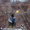 Photo showing a man sitting on the edge of a helicopter installing a SpanGuard ABS power line marker on a power line.