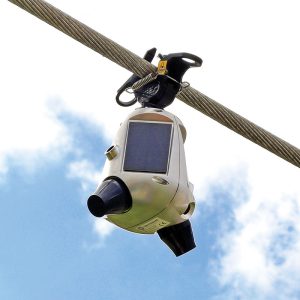 Photo showing a Sentrisense powerline monitoring unit mounted to a power line against a blue sky background.